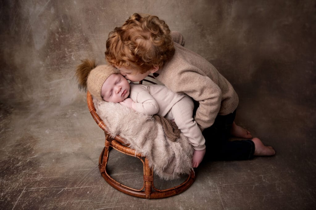 Older brother kissing newborn baby in studio basket portrait by Jamie Englert Photography in Glen Mills, PA.