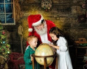 Santa and two children look at a globe while imagining Santa’s Christmas Eve journey around the world.