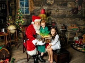 Santa reads a Christmas story with two children during an interactive Santa photography session.