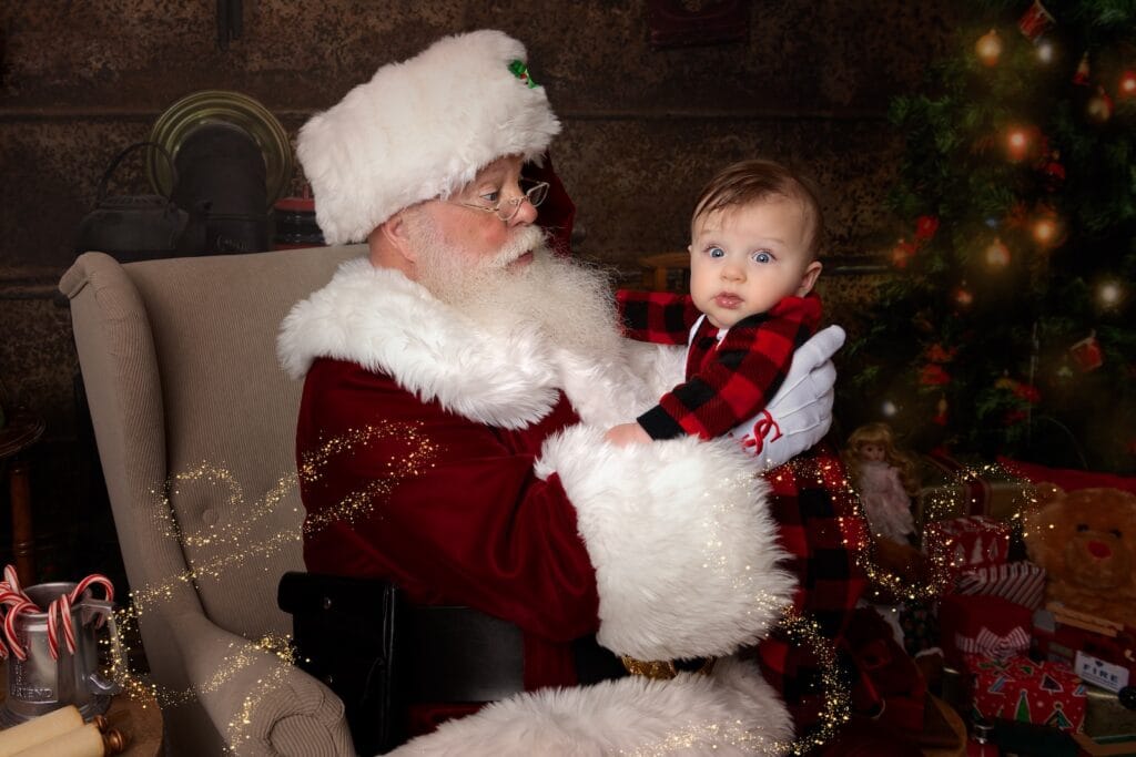 Santa holding a baby in red plaid pajamas during a Christmas portrait session serving Main Line families.