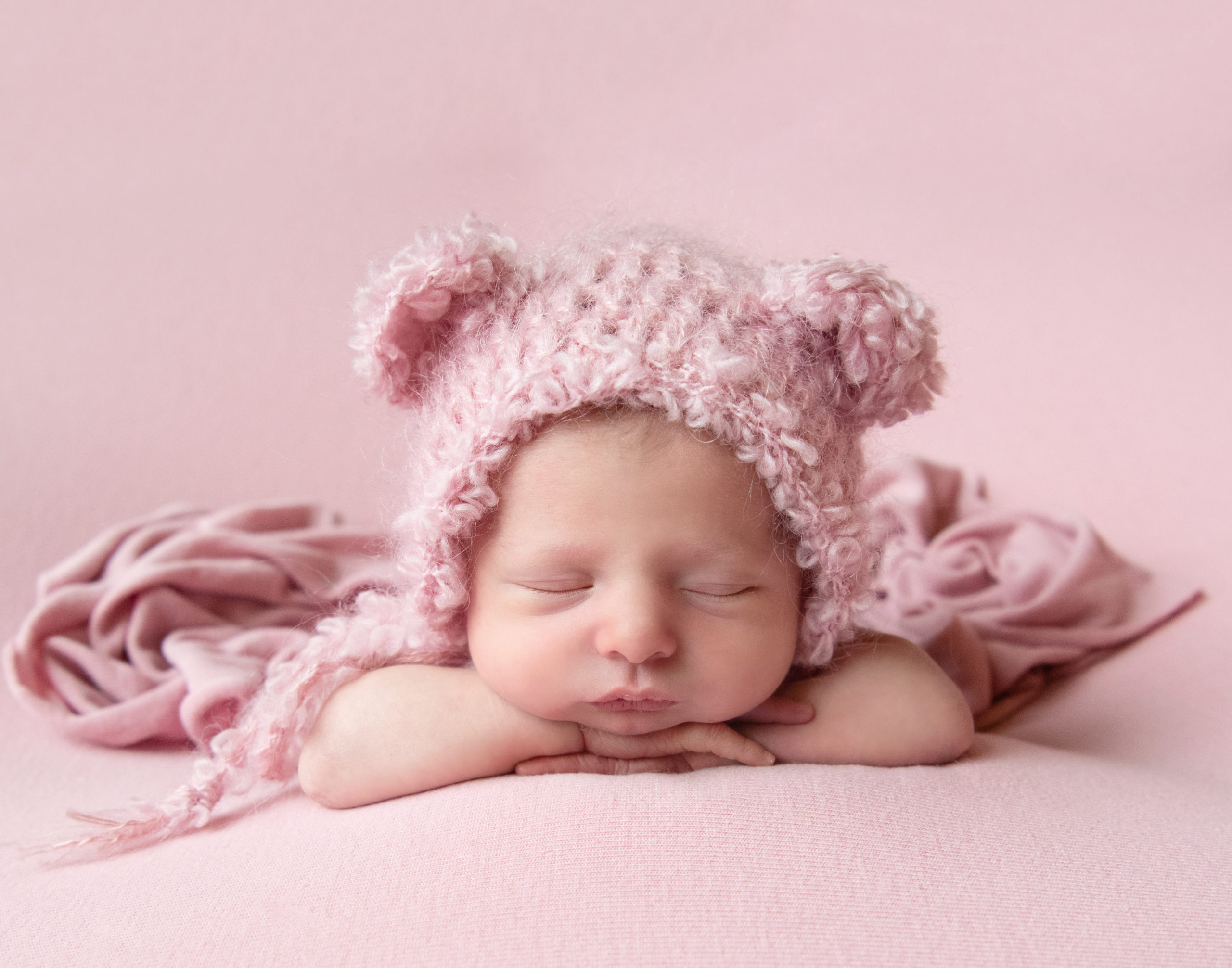 Newborn girl resting on her arms sleeping, cute pink bonnet